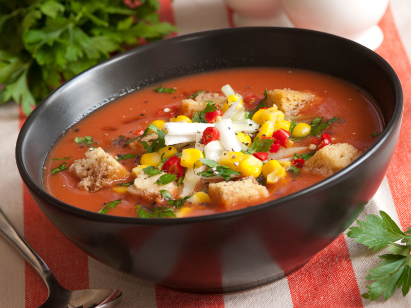 bowl of gazpacho with lots of toppings like cheese, corn, croutons and more