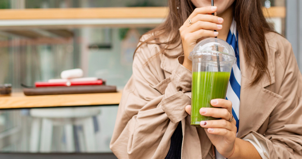 woman drinking a plastic cup of green gazpacho with a straw