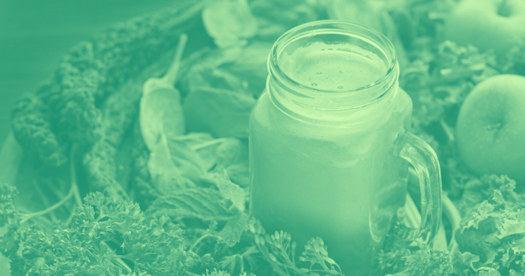 greengazpacho in a jar surrounded by kale adn other green vegetables with a duoton green filter